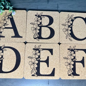May include: Six cork coasters with black floral designs and the letters A, B, C, D, E, and F.