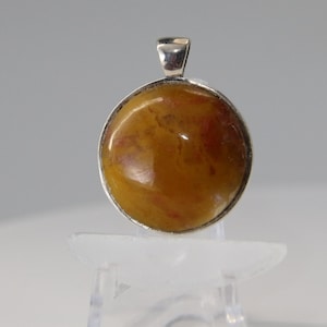 May include: A round silver pendant with a yellow and red agate stone.