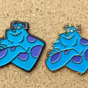 Può includere: Due spille in smalto blu e viola del personaggio Sulley del film Monsters & Co. Le spille hanno la forma di Sulley seduto con le braccia incrociate. Una spilla ha un contorno nero e l'altra un contorno dorato.