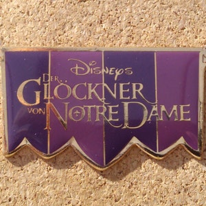 Op de afbeelding: Een rechthoekige pin met een gouden rand en een paarse en donkerpaarse achtergrond. De pin heeft de tekst "Disney's Der Glockner von Notre Dame" in gouden letters. De pin heeft decoratieve gouden accenten in elke hoek.