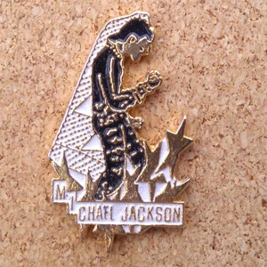 K&ouml;nnte beinhalten: Goldfarbene Anstecknadel mit einem schwarz-wei&szlig;en Cartoon-Bild von Michael Jackson in einem schwarzen Anzug und wei&szlig;em Handschuh, der auf einem wei&szlig;en und goldenen Stern kniet. Der Text "MICHAEL JACKSON" ist in wei&szlig;en Buchstaben auf einem goldenen Banner geschrieben.