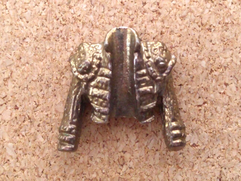 K&ouml;nnte beinhalten: Eine goldfarbene Metalljacke-Anstecknadel mit einem detaillierten Design. Die Jacke hat einen hohen Kragen und einen dekorativen Besatz an den R&auml;ndern.