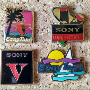 Könnte beinhalten: Vier Vintage-Anstecknadeln mit dem Sony-Logo. Zwei Anstecknadeln zeigen eine Palme und eine Ozeanszene mit dem Text "Sony Tape". Eine Anstecknadel zeigt ein schwarzes und rotes Sony Walkman-Logo. Eine Anstecknadel zeigt ein schwarzes und rotes Sony V-Logo.