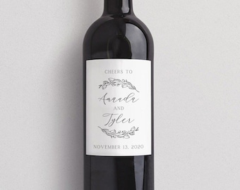 May include: A white wine bottle label with a black floral wreath design. The label reads "Cheers to Amanda and Tyler, November 11, 2020".