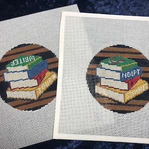 May include: Two needlepoint canvases with a circular design featuring a stack of books. The books are in various colors, including red, blue, green, and yellow, with the word "WRITER" and "HOIFT" visible. The background is a brown circle with horizontal stripes.
