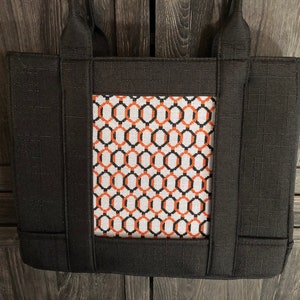 May include: Black tote bag with a geometric pattern in orange, black, and white on the front.