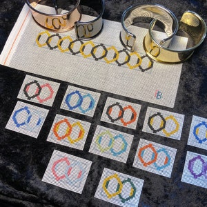 May include: A set of 10 colorful embroidered canvas patches featuring the Olympic rings symbol. The patches are arranged in a grid pattern on a black fabric background. The rings are in various colors, including red, blue, yellow, green, and black.