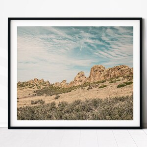 May include: A scenic landscape photograph featuring a rocky hillside with a blue sky and white clouds in the background.