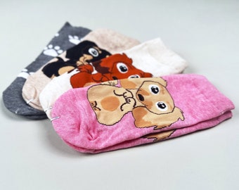 May include: Four pairs of colorful socks with cartoon animal designs. The socks are folded and stacked on top of each other. The top sock is pink with a brown and white dog design. The second sock is beige with a brown fox design. The third sock is beige with a black and white cat design. The bottom sock is gray with white paw prints.