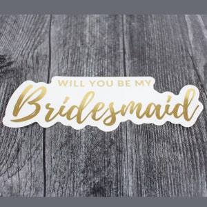 May include: White card with gold lettering that says "Will you be my Bridesmaid?"
