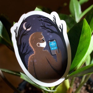 May include: A sticker featuring a brown, furry creature wearing a blue face mask and holding a smartphone with the text "NO STRANGERS + U = THE SQUAD" on the screen. The creature is standing in a dark forest with trees and a crescent moon in the background.