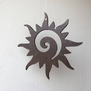 May include: A rusty metal sun with a spiral design hanging from a white string. The sun is a decorative piece with a rustic look.