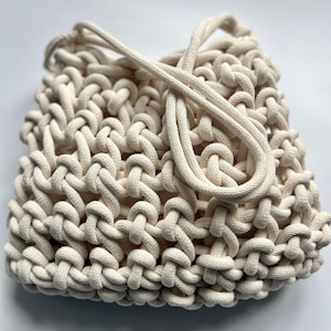 May include: A white crocheted tote bag with thick rope handles. The bag is made of a tightly woven, open-weave pattern.