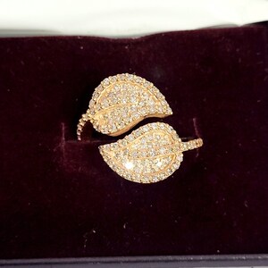 May include: A gold ring with two leaves set with sparkling diamonds. The leaves are connected by a thin band.