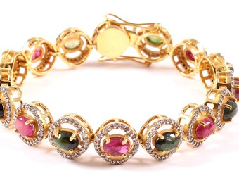 May include: A gold bracelet with oval-shaped gemstones in shades of pink, green, and black. The gemstones are set in a gold frame with smaller diamonds surrounding them.