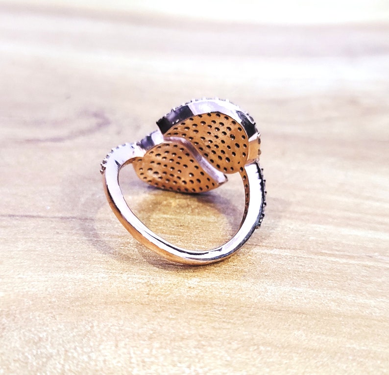 May include: A rose gold ring with two interlocking heart-shaped settings, each set with small sparkling stones.