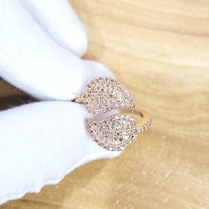 May include: A rose gold ring with two leaf-shaped bands set with sparkling diamonds.