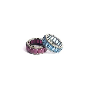 May include: Two silver rings with a row of rectangular gemstones. One ring has blue gemstones and the other has red gemstones.