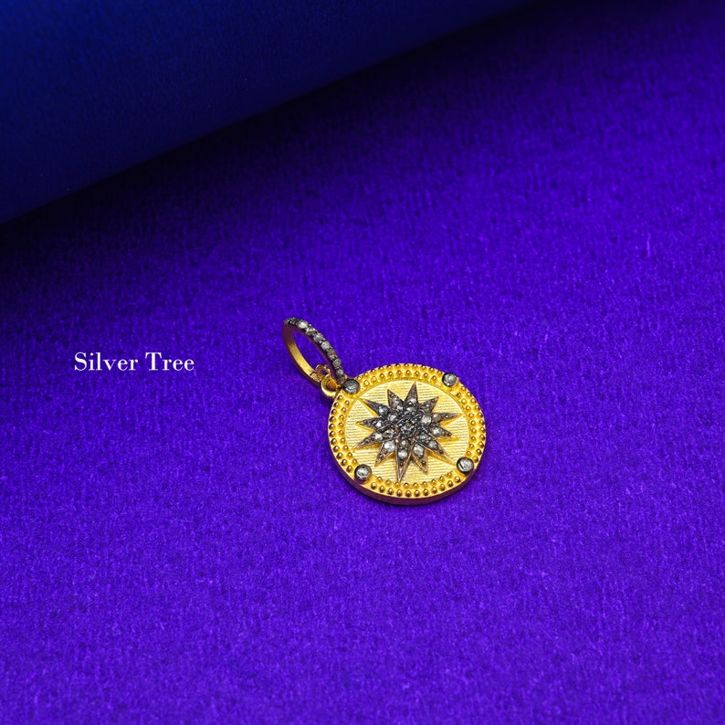 May include: A gold pendant with a starburst design set with black diamonds. The pendant is on a purple background.