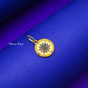 May include: A gold pendant with a starburst design set with black diamonds. The pendant is on a blue background.
