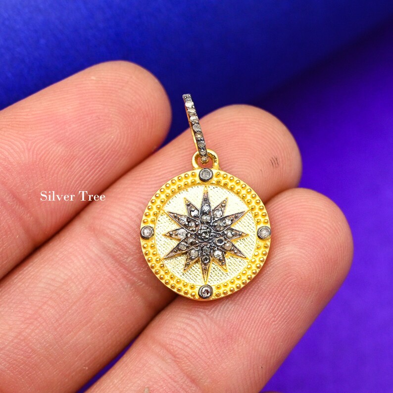 May include: A gold pendant with a round, star-shaped design. The star is made of small, white diamonds and is surrounded by a circle of smaller, black diamonds. The pendant is on a gold chain.