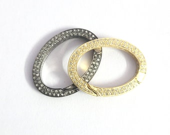 May include: Two oval-shaped jewelry clasps. One is gold-toned, the other is dark gray. Both clasps are encrusted with small, sparkling stones. The clasps are interlocked, suggesting they are designed to connect jewelry pieces.