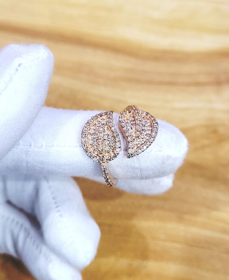 May include: A gold ring with two leaf-shaped designs set with clear stones.