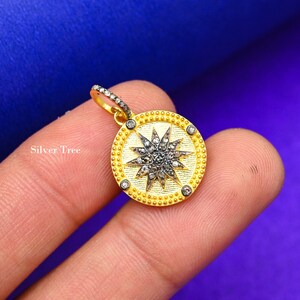 May include: A gold pendant with a silver starburst design set with small diamonds. The pendant is round and has a beaded border.