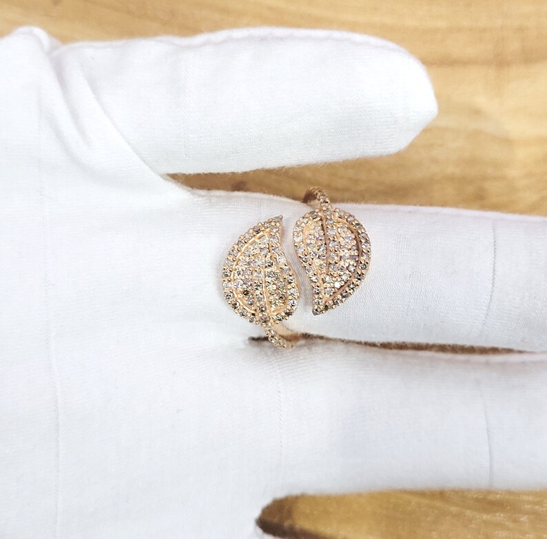 May include: A gold ring with two leaf-shaped designs, each set with sparkling clear stones.