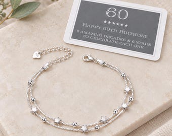 May include: A double-strand silver bracelet featuring alternating small round beads and star-shaped charms, with a lobster clasp and a heart-shaped tag marked 925. Accompanied by a rectangular card reading 60 HAPPY 60TH BIRTHDAY 6 AMAZING DECADES & 6 STARS TO CELEBRATE EACH ONE.