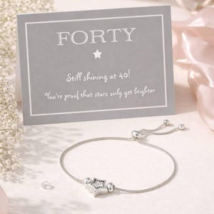 May include: A silver bracelet with a star-shaped charm and a card that reads "FORTY" with the text "Still shining at 40! You're proof that stars only get brighter."