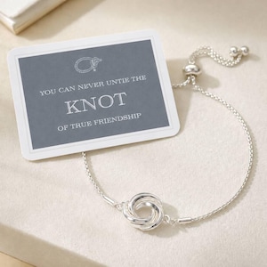 May include: A silver-toned chain bracelet featuring a central knot charm, accompanied by a rectangular card with a dark gray background and white text that reads: YOU CAN NEVER UNTIE THE KNOT OF TRUE FRIENDSHIP, along with a small line-art knot icon.