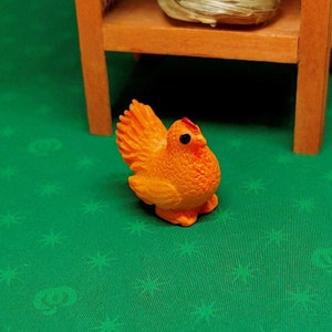 May include: Orange plastic toy chicken with a textured surface. The chicken has a red comb and black eyes.