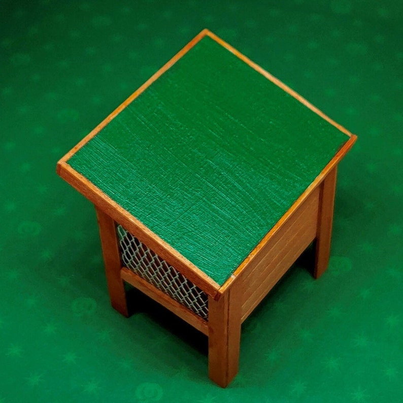 May include: A small wooden birdhouse with a green roof. The birdhouse has a wire mesh front and is sitting on a green surface.
