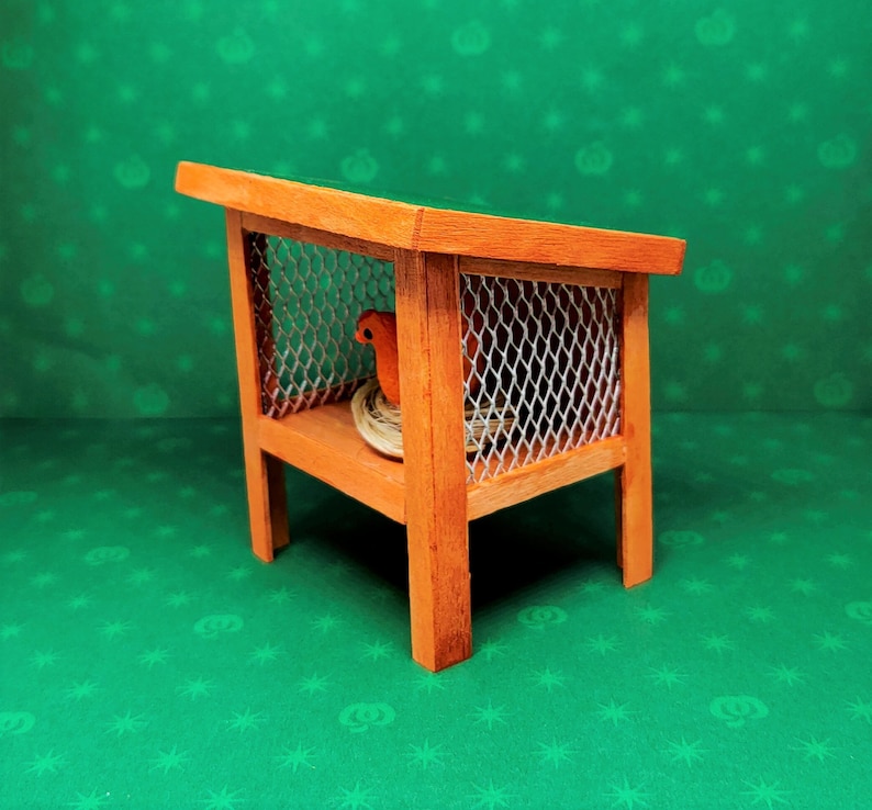 May include: A wooden birdhouse with a wire mesh cage and a small orange bird figurine inside. The birdhouse is on a green background.
