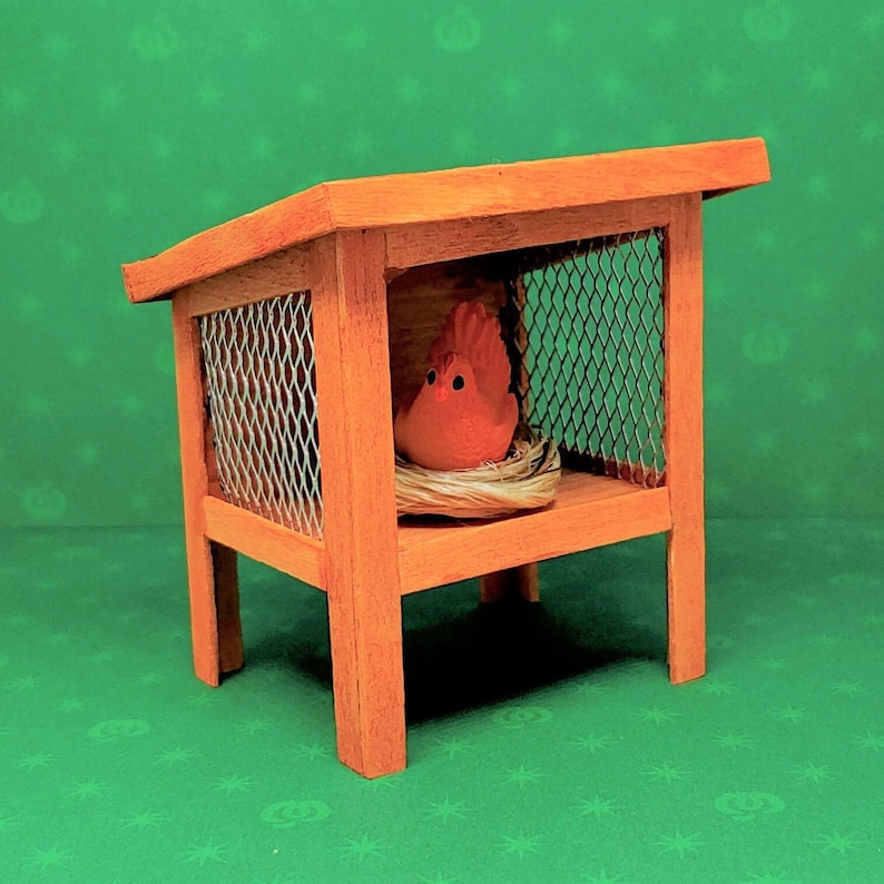 May include: A small wooden birdhouse with a wire mesh cage and a red bird figurine inside. The birdhouse is sitting on a green surface.