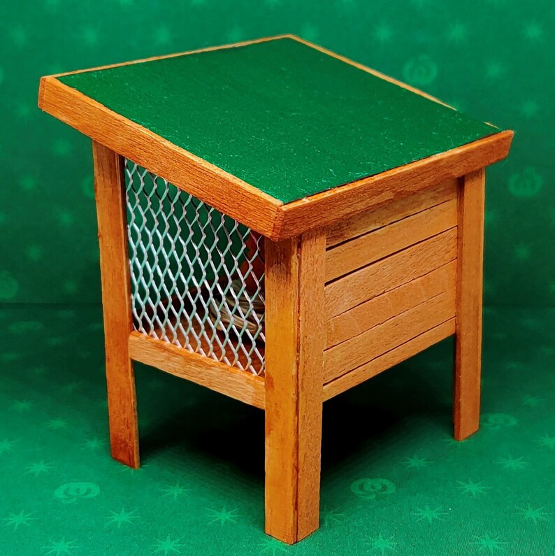 May include: A small wooden pet house with a green felt roof and a wire mesh front. The house is on a green background.