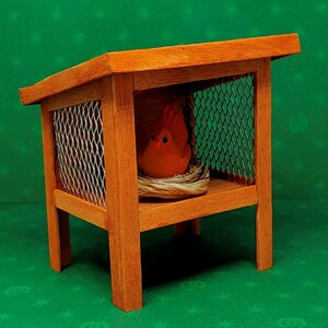 May include: A wooden birdhouse with a wire mesh front and a small orange bird figurine inside. The birdhouse has a brown wood finish and a pitched roof.