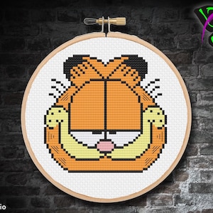 May include: A cross-stitch pattern of Garfield the cat, with his signature orange fur, black eyes, and a pink nose. He is shown with his arms crossed over his chest, looking slightly annoyed.