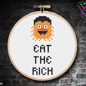 May include: A white embroidery hoop with a cross-stitch design featuring a cartoon character with orange hair and the text "EAT THE RICH".