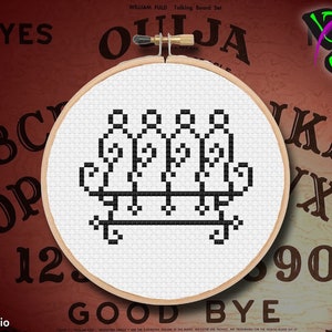 以下が含まれることがあります： 白地に黒のクロスステッチで五芒星が描かれたパターン。クロスステッチは木製の刺繍枠に入っています。枠は、赤い背景に黒い文字で「YES」、「ABC」、「NOP」、「12」、「GOOD BYE」、「OUIJA」、「KLM」、「XYZ」、「90」と書いてあります。