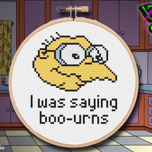 May include: A cross-stitch embroidery hoop with a yellow cartoon character with glasses and the text "I was saying boo-urns".