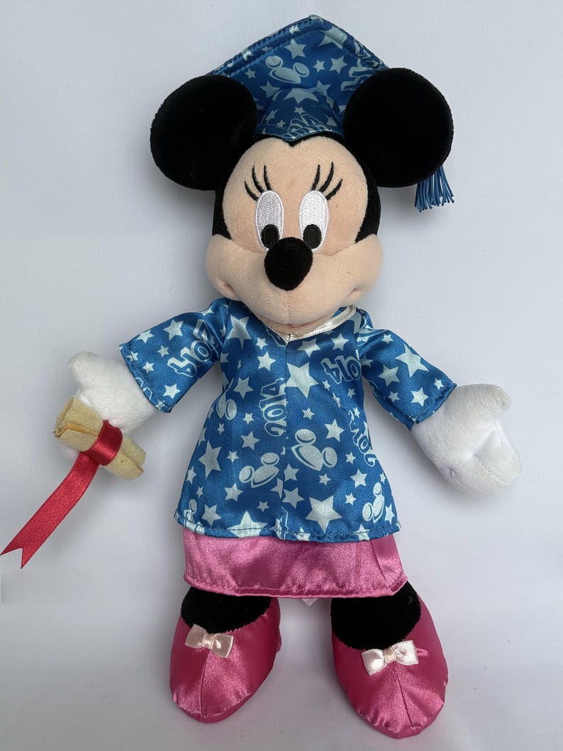 May include: A plush Minnie Mouse doll wearing a blue graduation cap and gown with white stars and Mickey Mouse silhouettes. The gown has the year "2014" printed on it. She holds a rolled diploma with a red ribbon and wears pink shoes.