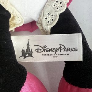 May include: Close-up of a Disney Parks plush toy. The toy has black, pink, and white elements. The tag reads "Disney Parks AUTHENTIC ORIGINAL &copy; Disney" with a castle logo.