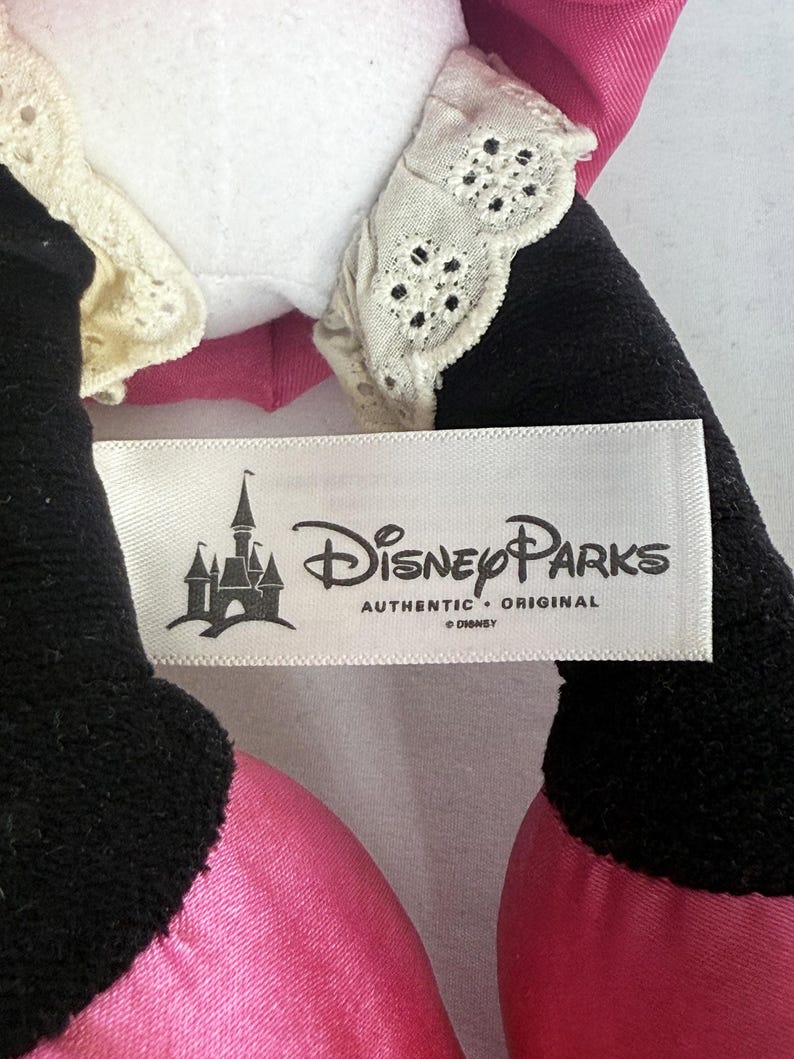 May include: Close-up of a Disney Parks plush toy. The toy has black, pink, and white elements. The tag reads "Disney Parks AUTHENTIC ORIGINAL &copy; Disney" with a castle logo.