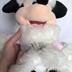 May include: A plush toy of Minnie Mouse wearing a pink and white winter coat with a silver trim. She has a black nose and large black eyes.