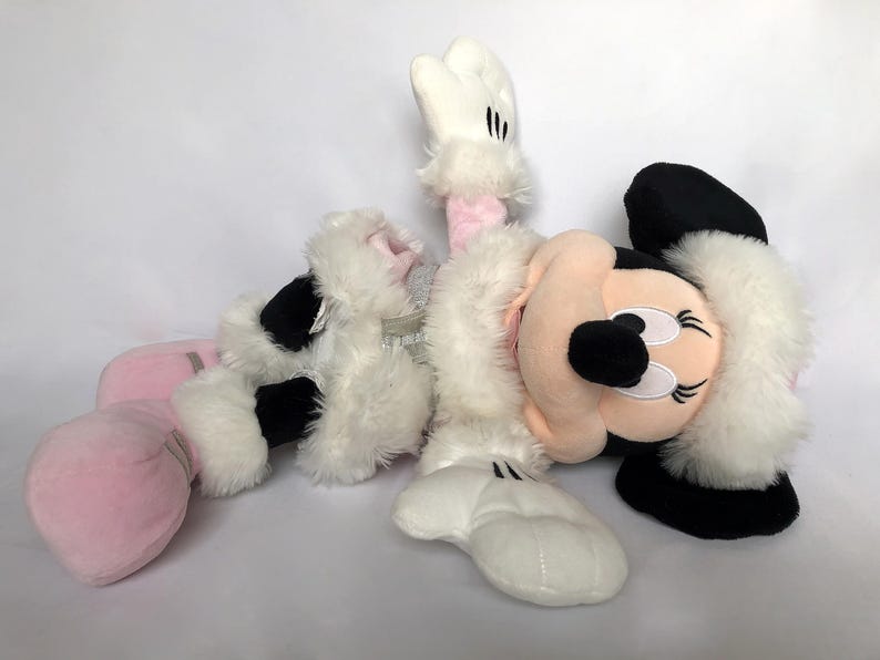 May include: A plush toy of Minnie Mouse dressed in a white and pink winter outfit with a white fur trim. She is wearing pink boots and has a black nose and eyes.