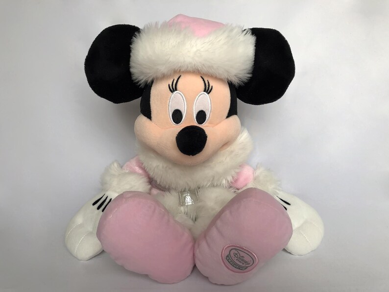 May include: A pink and white plush Minnie Mouse wearing a white fur trimmed hat and pink boots. The plush toy has a Disney logo on the bottom of one boot.