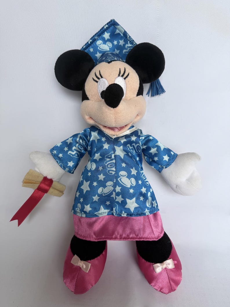 May include: A Minnie Mouse plush toy wearing a blue graduation gown with white stars and a matching cap. The plushie holds a diploma with a red ribbon and wears pink shoes with bows. The graduation gown has the text "2024".