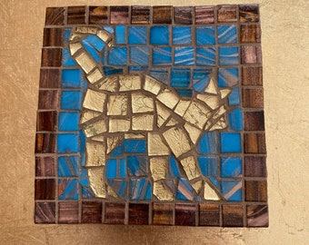 Puede incluir: Una obra de arte de mosaico de un gato, con azulejos dorados y azules, enmarcada en madera oscura.